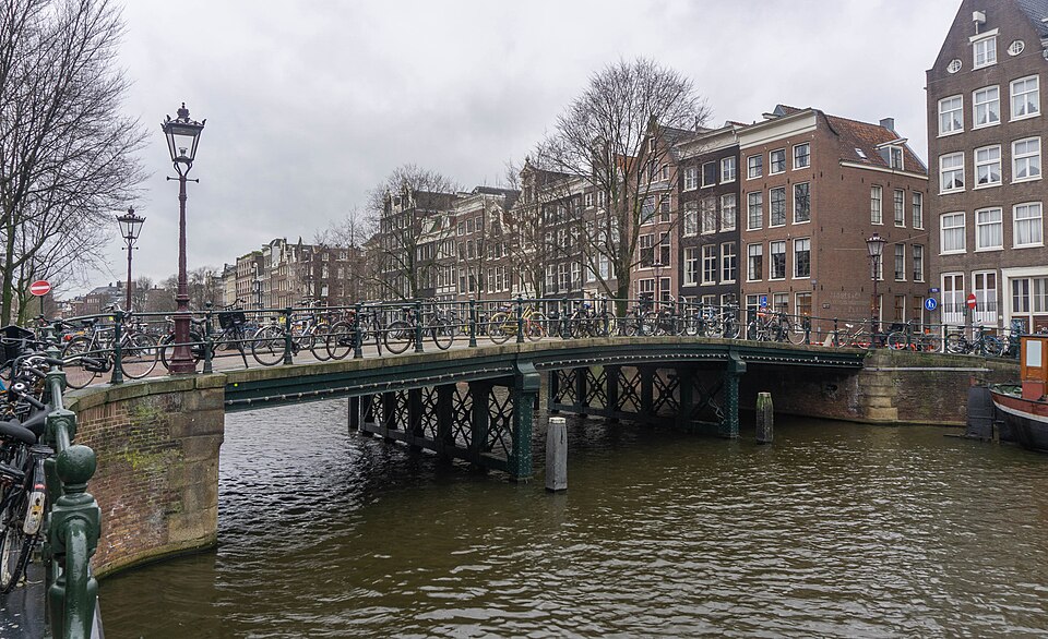 A bridge lined with bicycles beside Amsterdam canal houses.